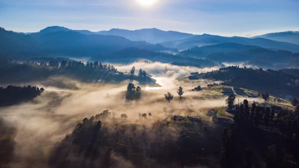 Aerial view of mountain valley blanketed in morning mist with layered hills and sunlight
